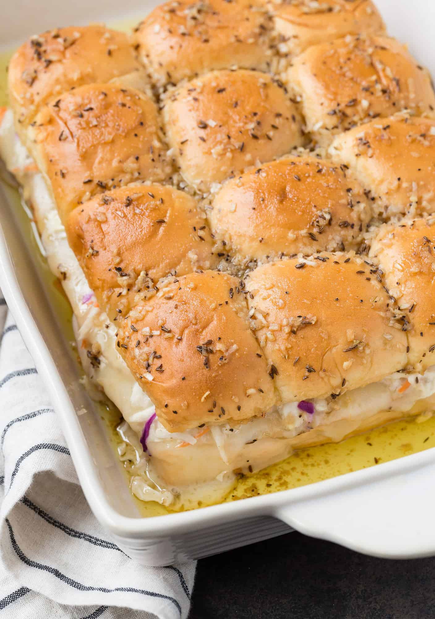 Rachel Sandwich sliders baked in a white baking dish, topped with caraway seeds.