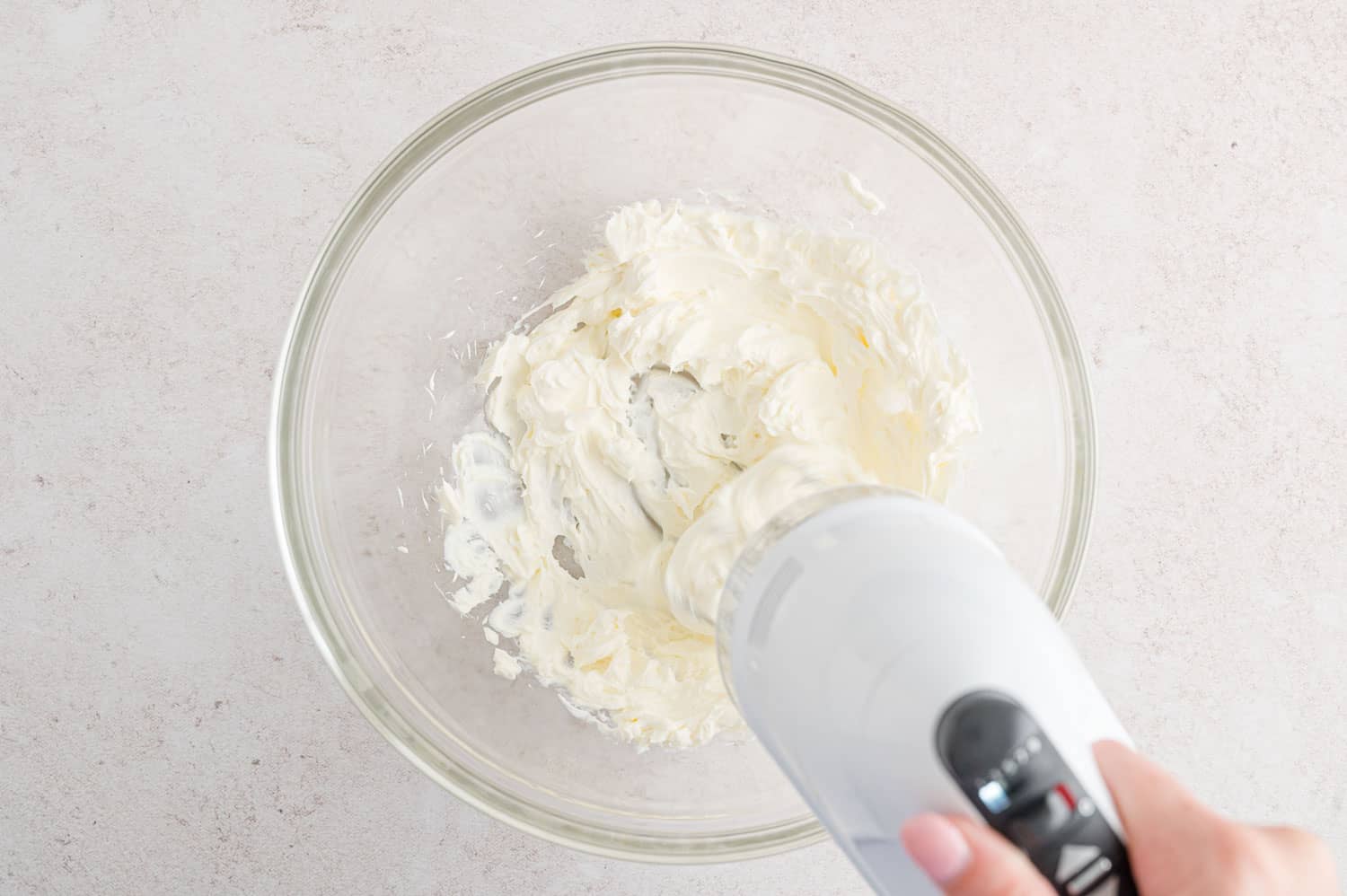 Cream cheese being whipped with an electric mixer.