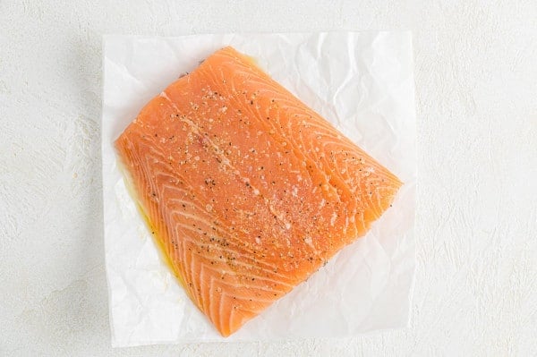 Overhead view of a seasoned uncooked salmon filet on a piece of parchment paper.