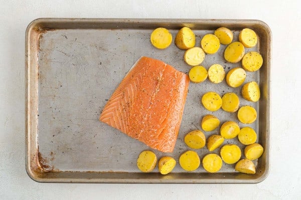 Overhead view of a seasoned salmon filet next to roasted potatoes on a sheet pan.