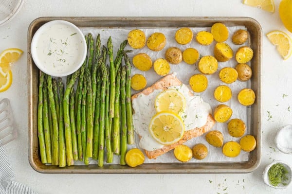 Overhead view of a salmon sheet pan dinner with asparagus and potatoes next to a salmon filet topped with lemon dill sauce.