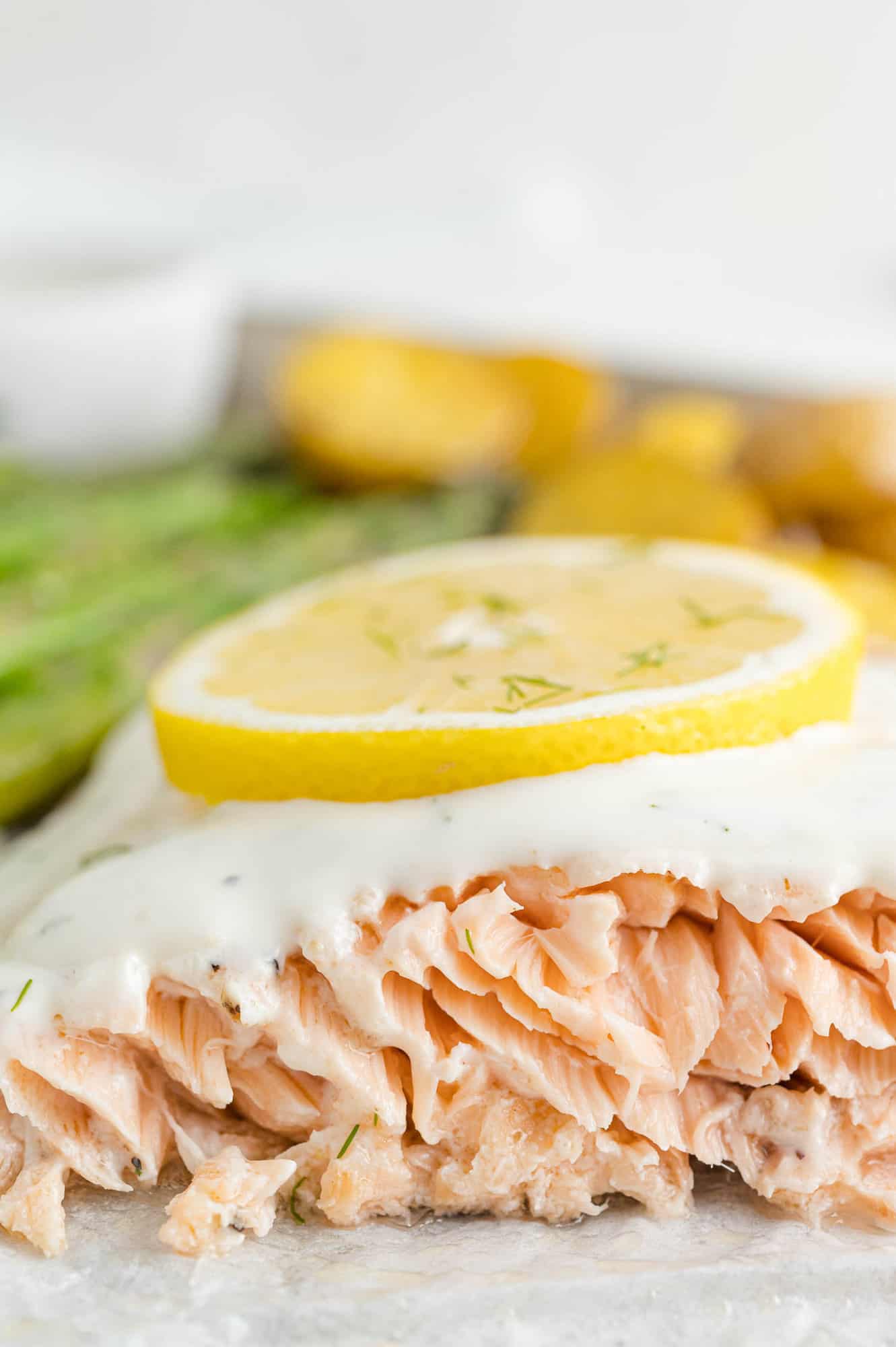 Close up of salmon topped with lemon dill sauce and a slice of lemon on a sheet pan.