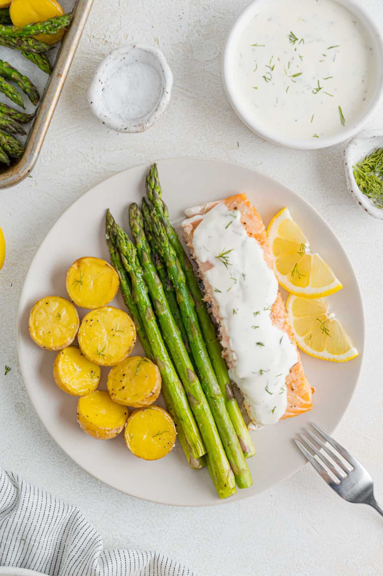 Overhead view of a plates salmon sheet pan dinner, with asparagus, potatoes, and salmon topped with lemon dill sauce.