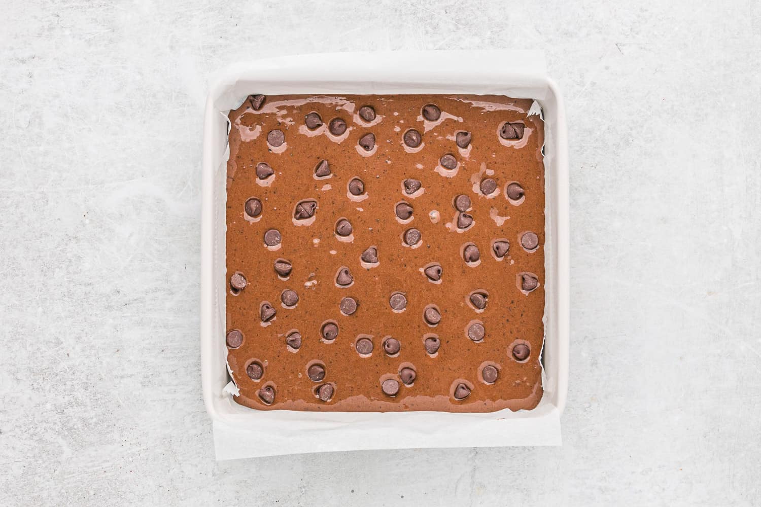 Chocolate chips sprinkled onto unbaked brownies.