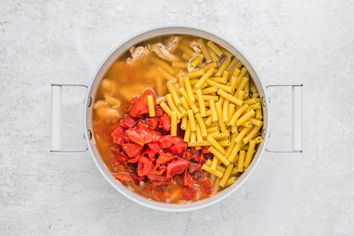 Uncooked pasta and tomatoes added to pan.
