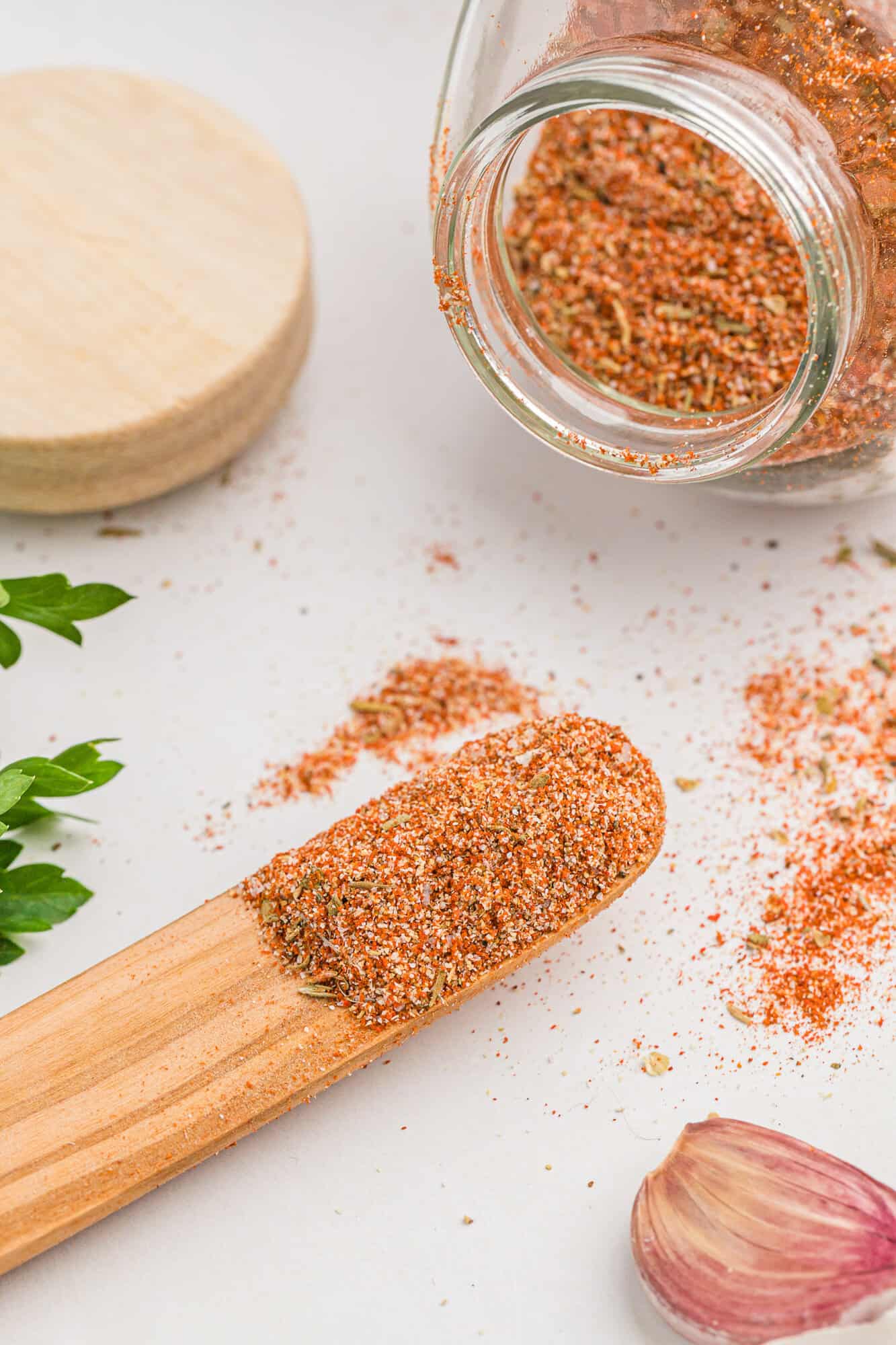 Cajun seasoning on a small wooden spoon and spilling out of a jar.