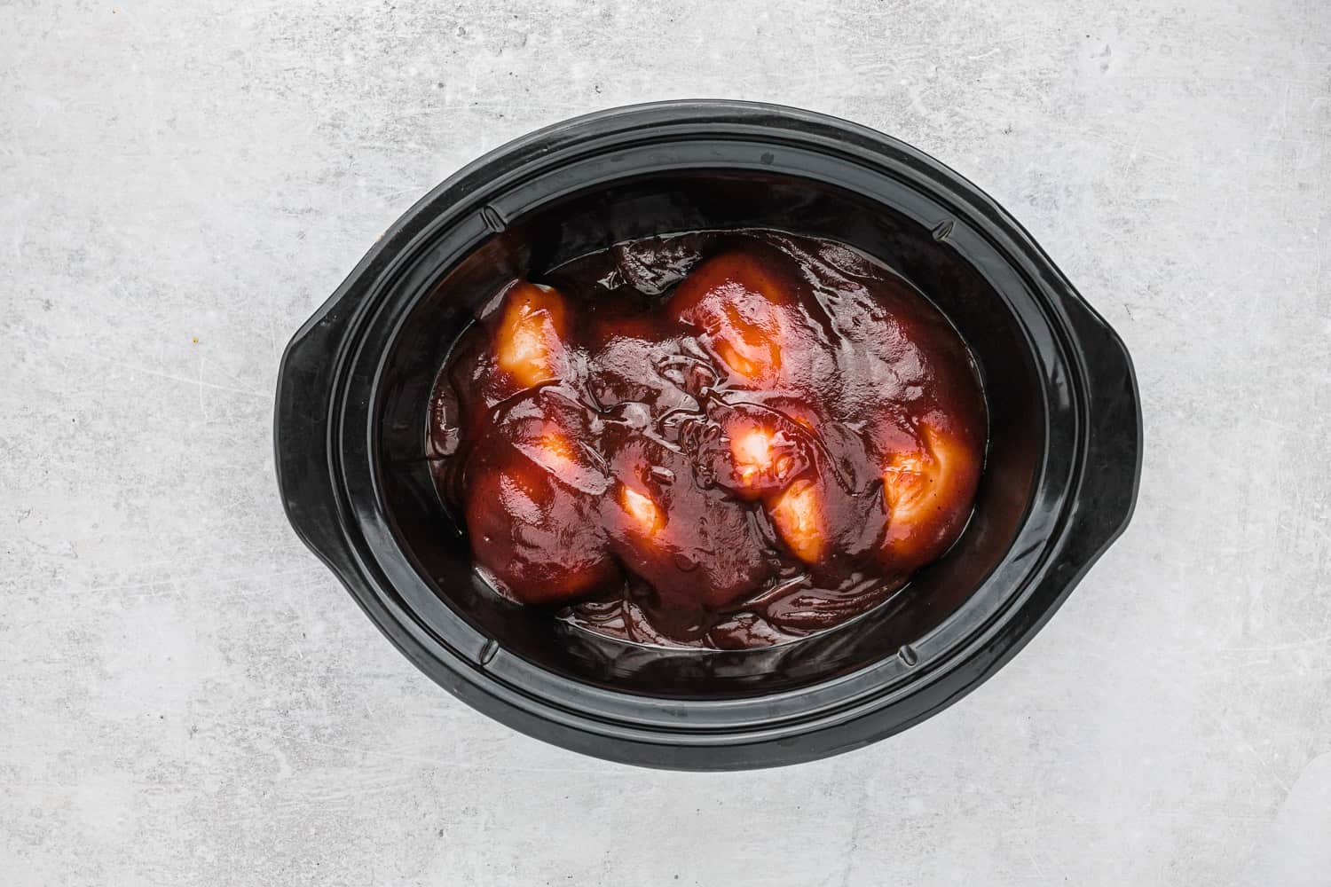 Uncooked chicken and bbq sauce in a slow cooker.