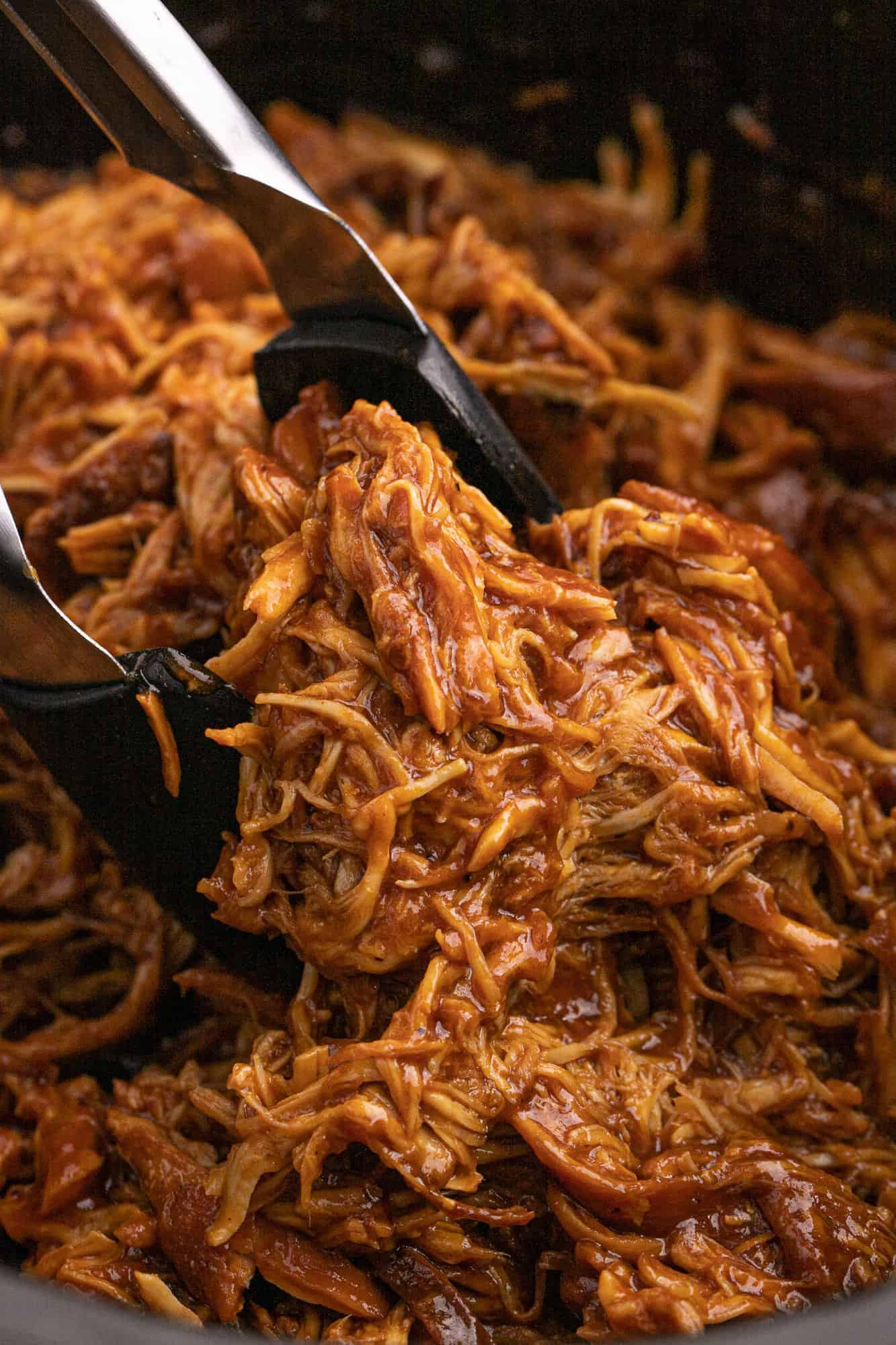 Slow Cooker BBQ chicken between tongs.