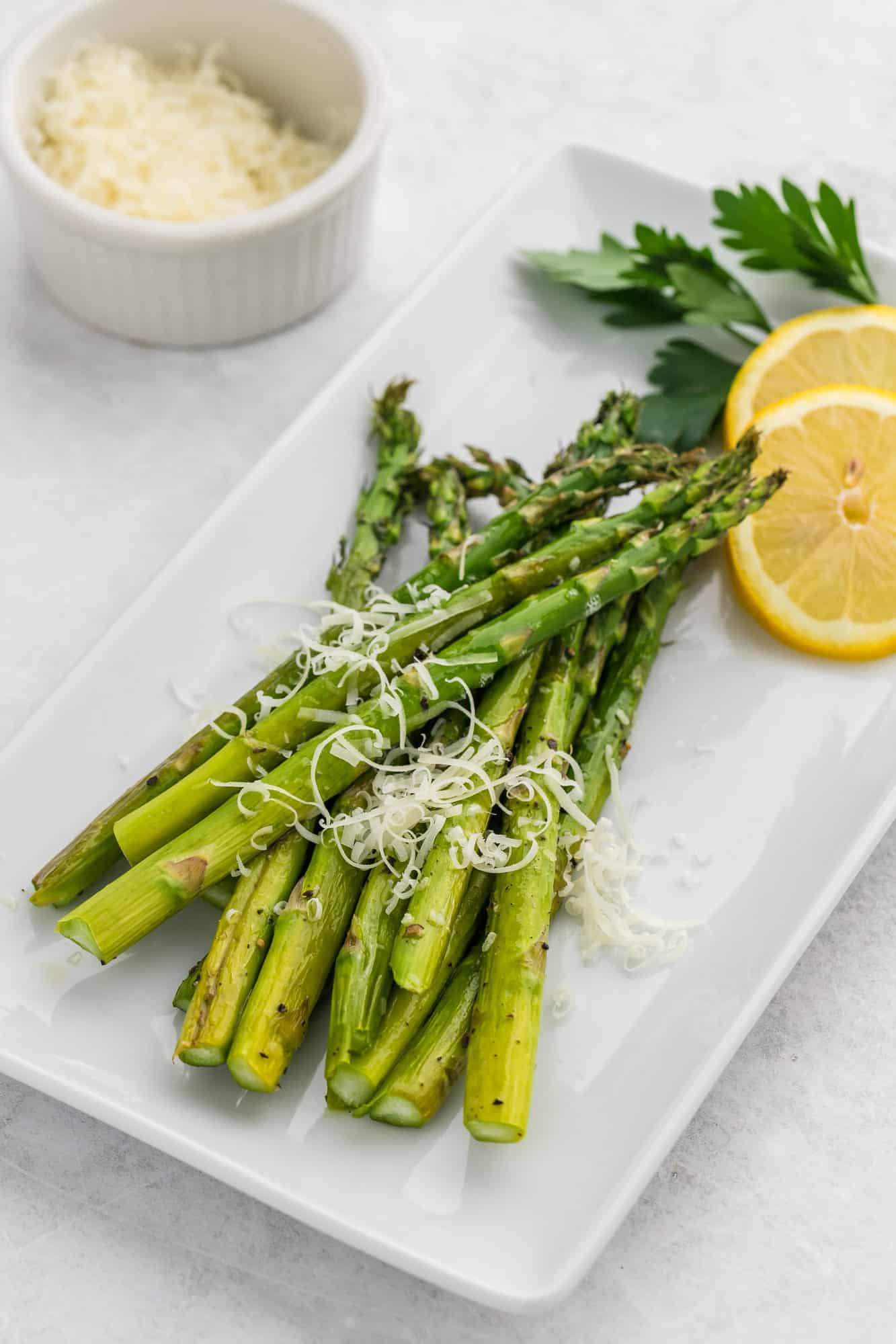 Roasted asparagus on a platter with parmesan cheese and lemon slices.