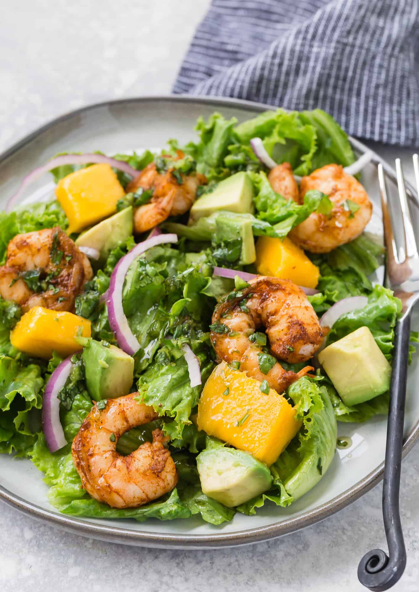 Shrimp salad with mango, avocado, red onion on a grey plate with a black fork.