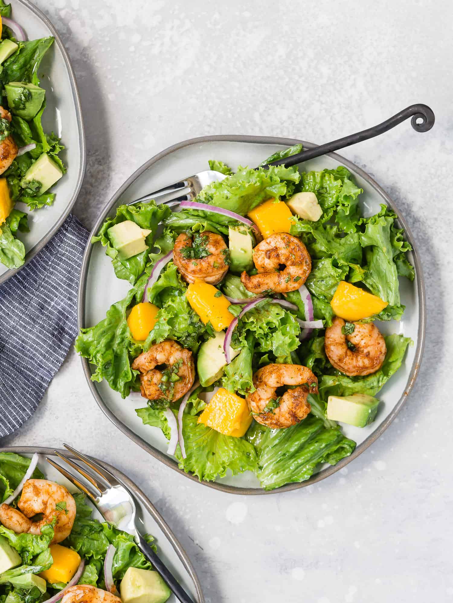 Overhead view of a bright green salad with mango, avocado, red onions, and shrimp.