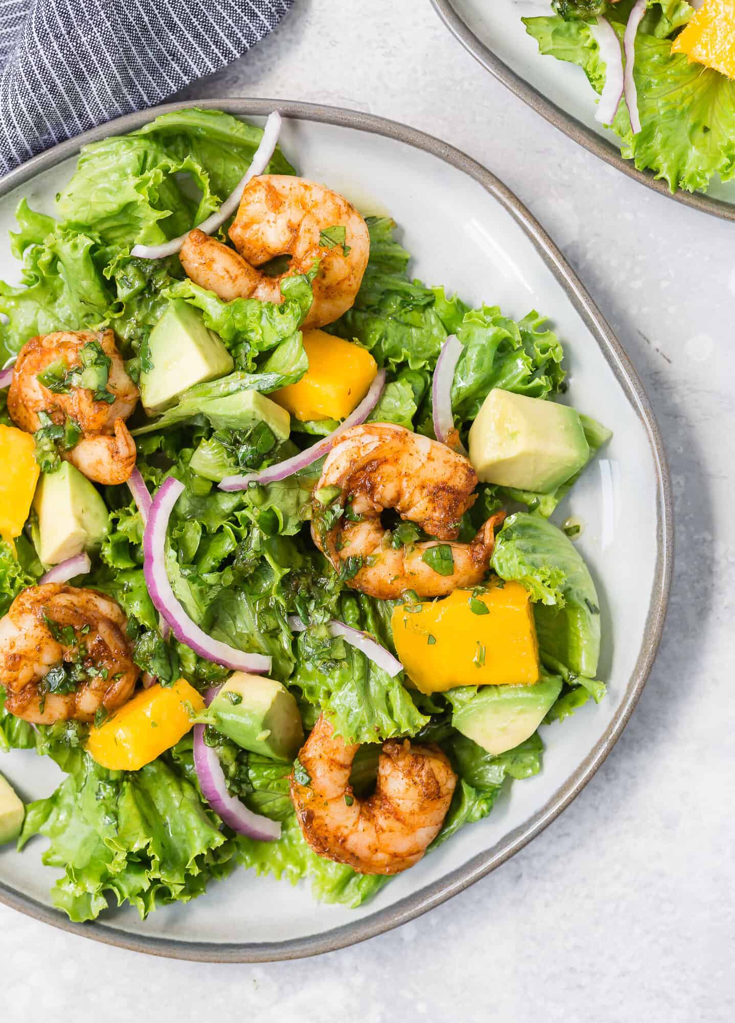 Overhead view of a bright green salad with mango, avocado, red onions, and shrimp.