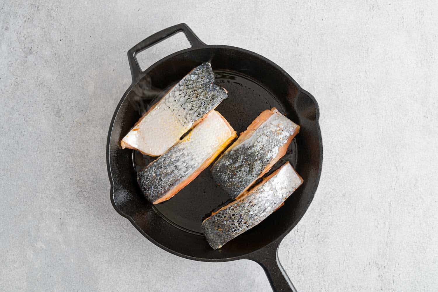 Salmon filets skin side up in a frying pan.