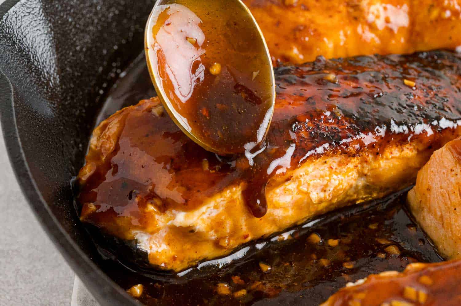 Orange glaze being spooned on salmon in a skillet.