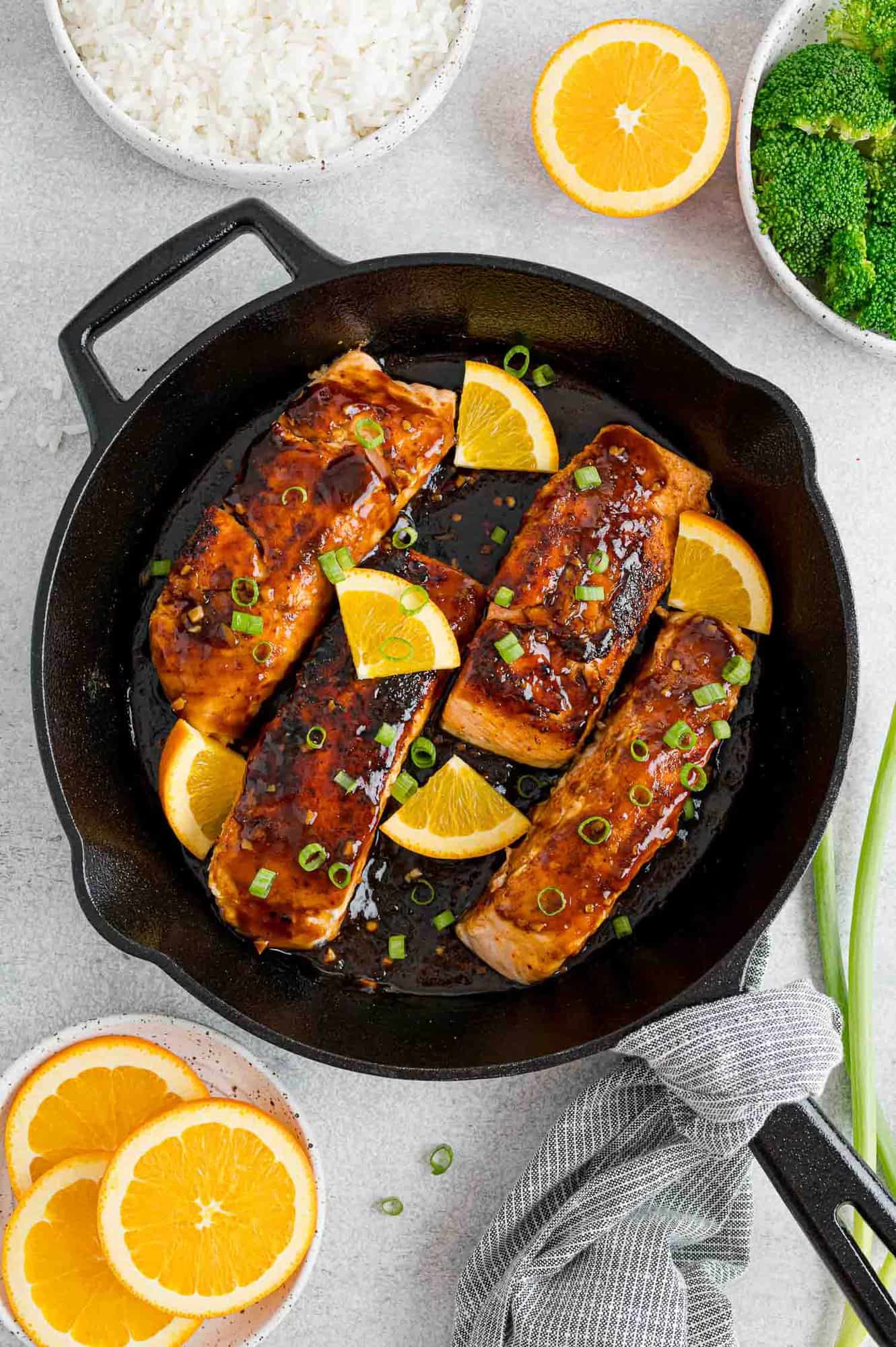 Overhead view of orange glazed salmon in a cast iron skillet topped with oranges and green onions.