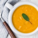 Squash soup in white bowl topped with sage.