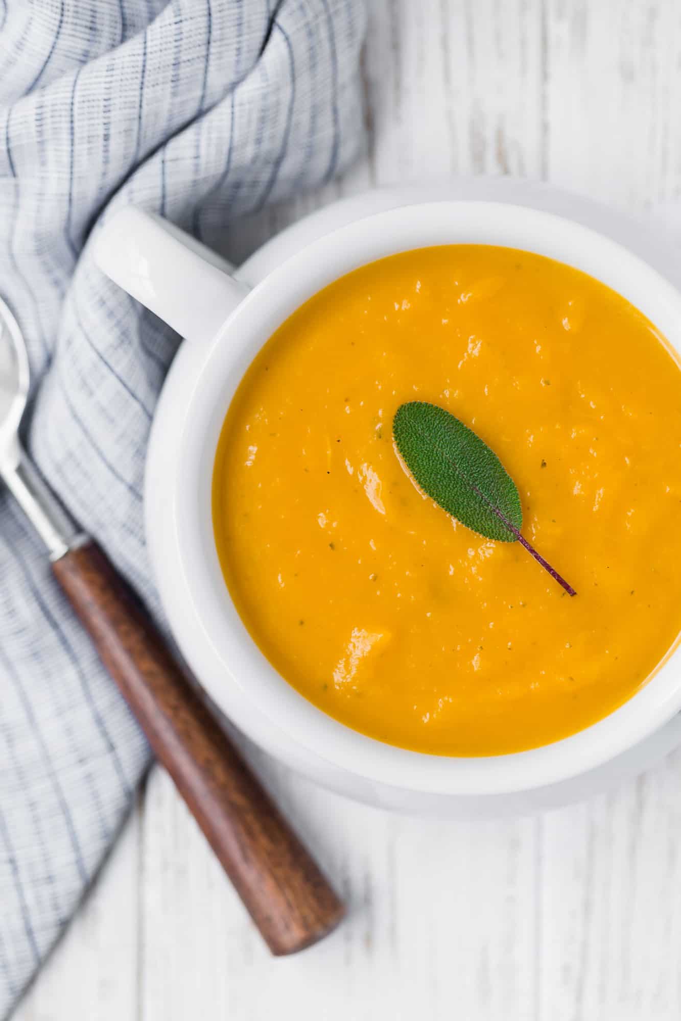 Squash soup in white bowl topped with sage.