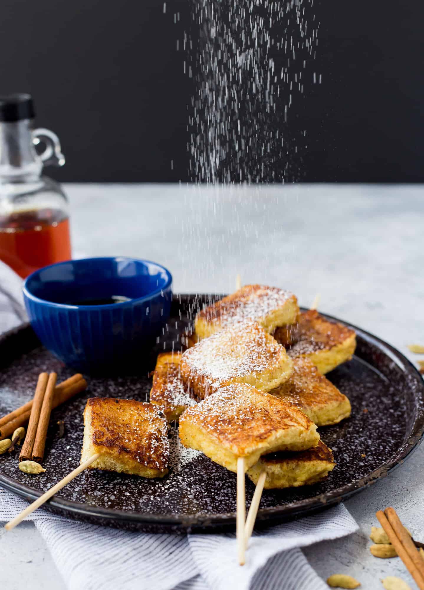 Powdered sugar being sprinkled on french toast skewers.