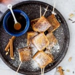 French toast skewers sprinkled with powdered sugar, maple syrup on side.