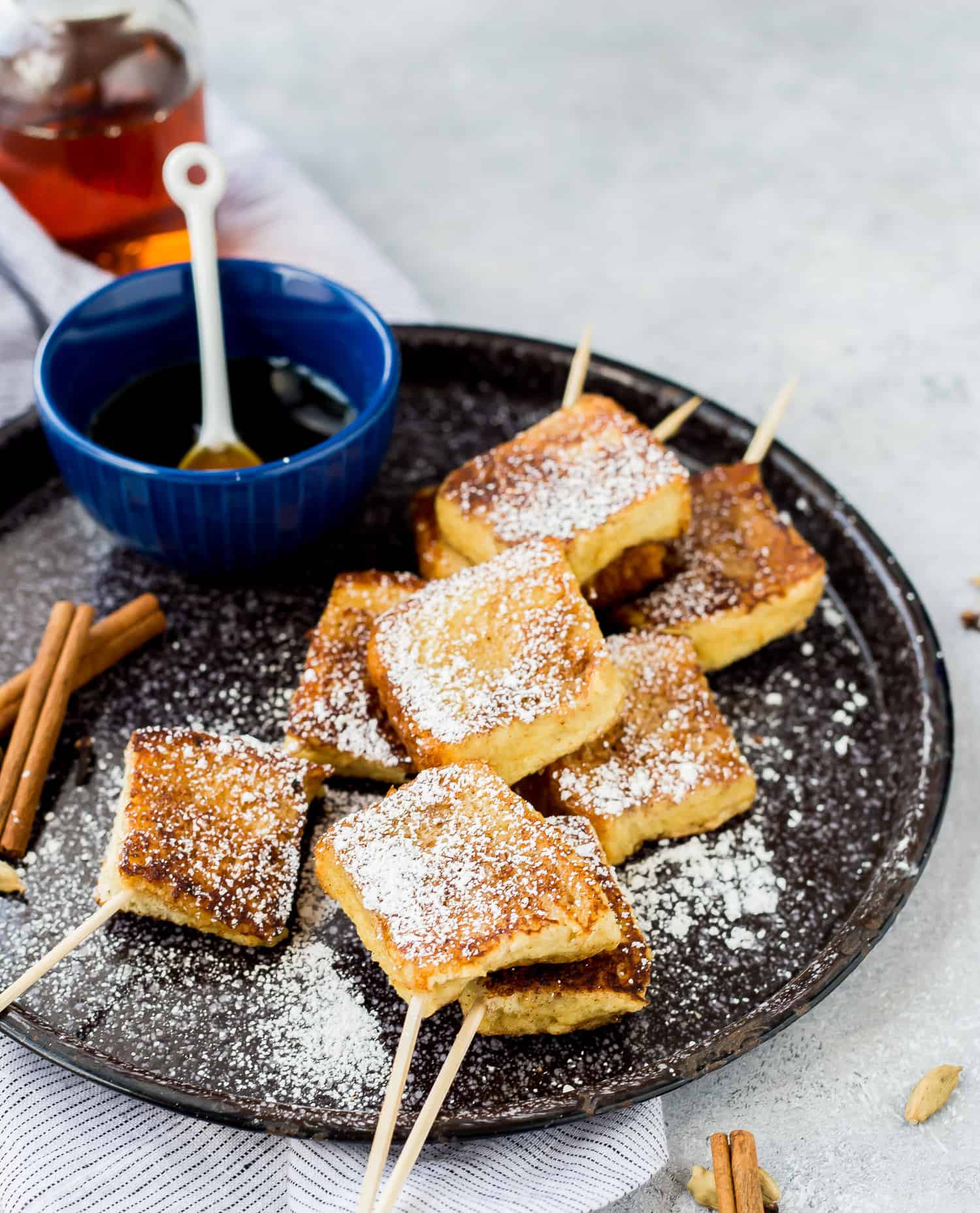 French toast skewers sprinkled with powdered sugar, maple syrup on the side.