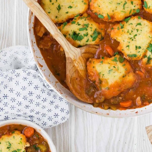 Chicken with cornmeal dumplings in a pan with spoon.