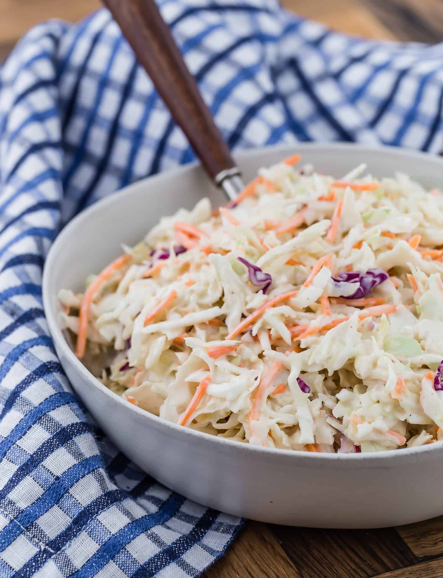 Creamy coleslaw in a bowl with wooden spoon.