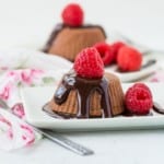 A small chocolate cheese cake on a white plate, with raspberries.