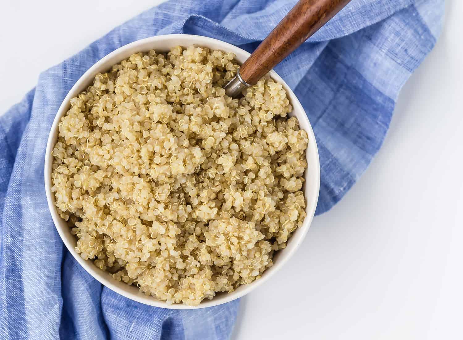Cooked quinoa in a bowl with a wooden spoon.