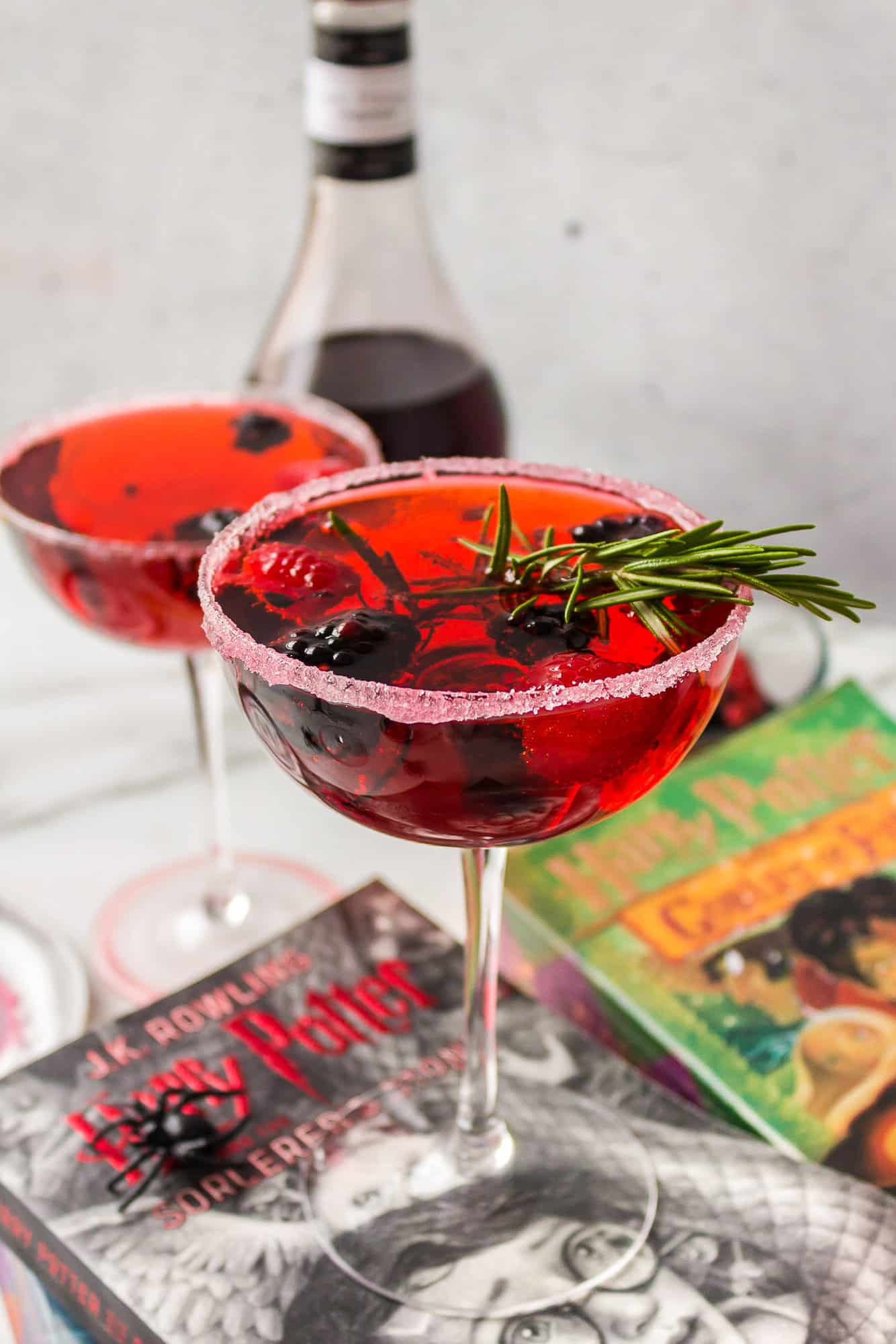 Two bright red cocktails with fruit and rosemary garnishes.