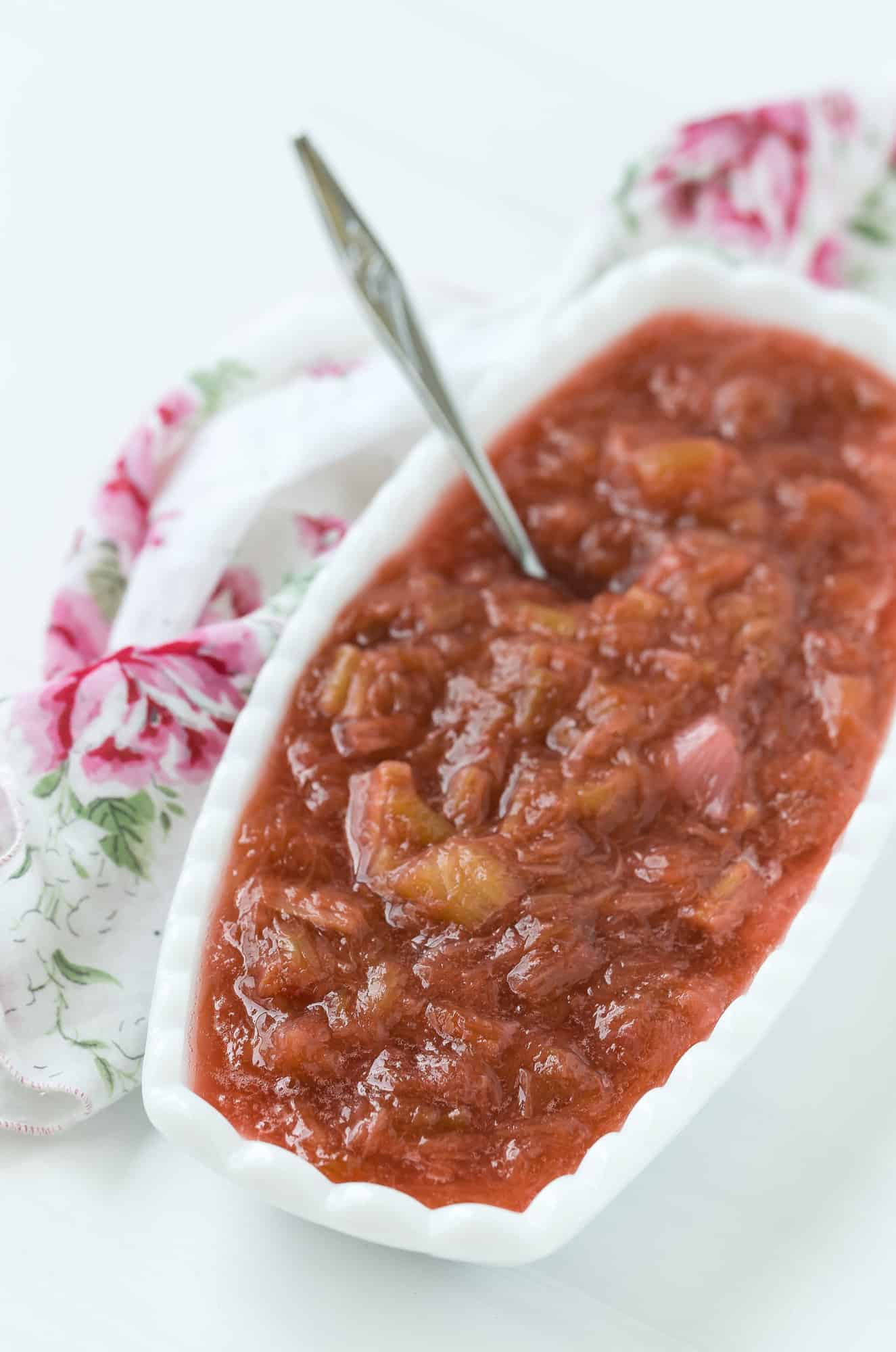 Light red rhubarb sauce in an oval shaped white bowl, with a spoon.