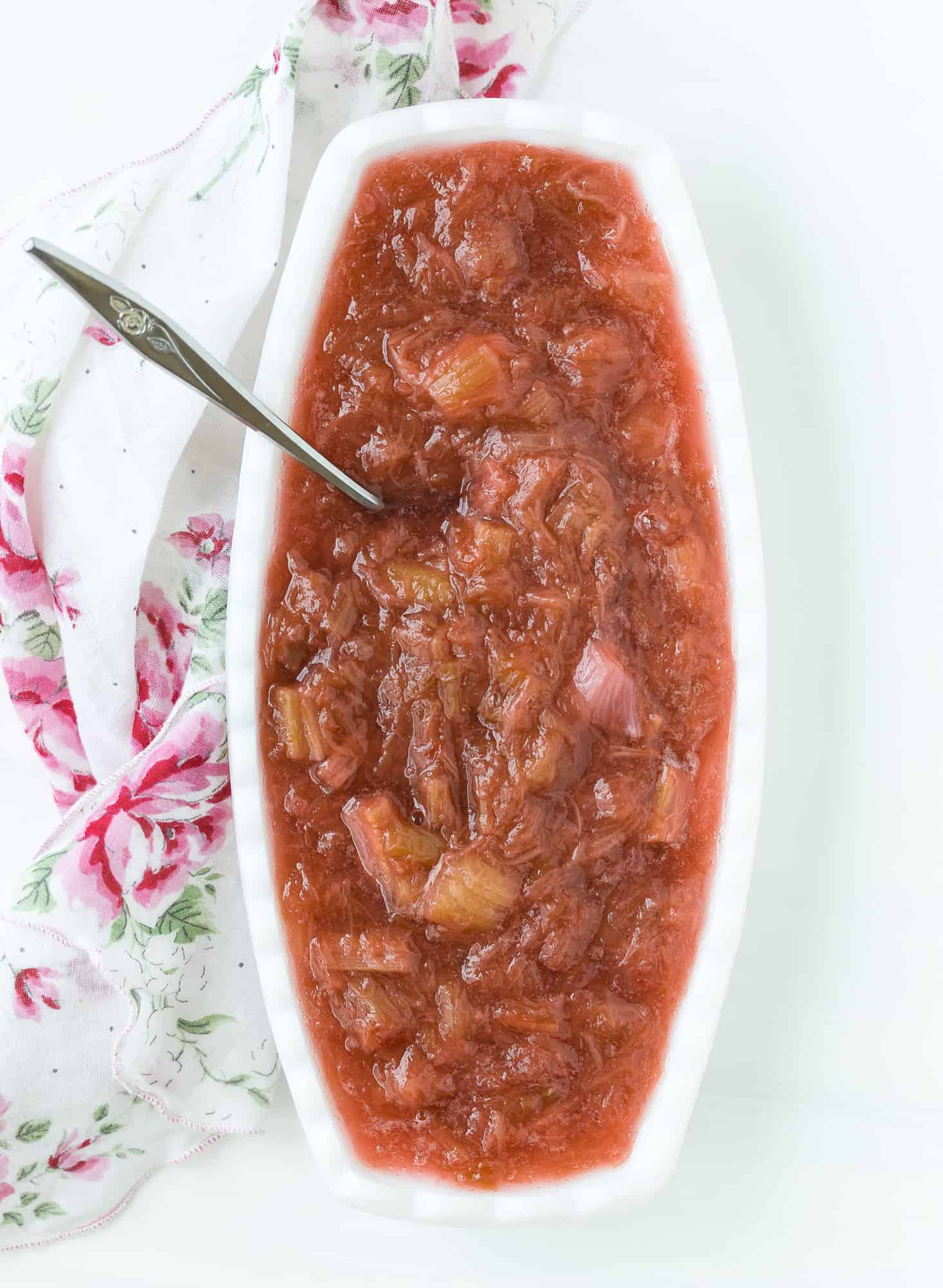 Rhubarb sauce in an oval shaped white bowl, with a silver spoon. 