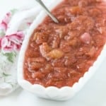 Light red rhubarb sauce in an oval shaped white bowl, with a silver spoon.