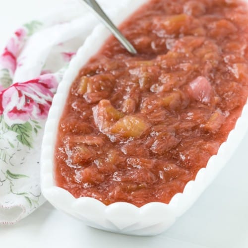Light red rhubarb sauce in an oval shaped white bowl, with a silver spoon.