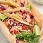 Salmon tacos with avocado slaw arranged on a serving plate next to lime wedges.