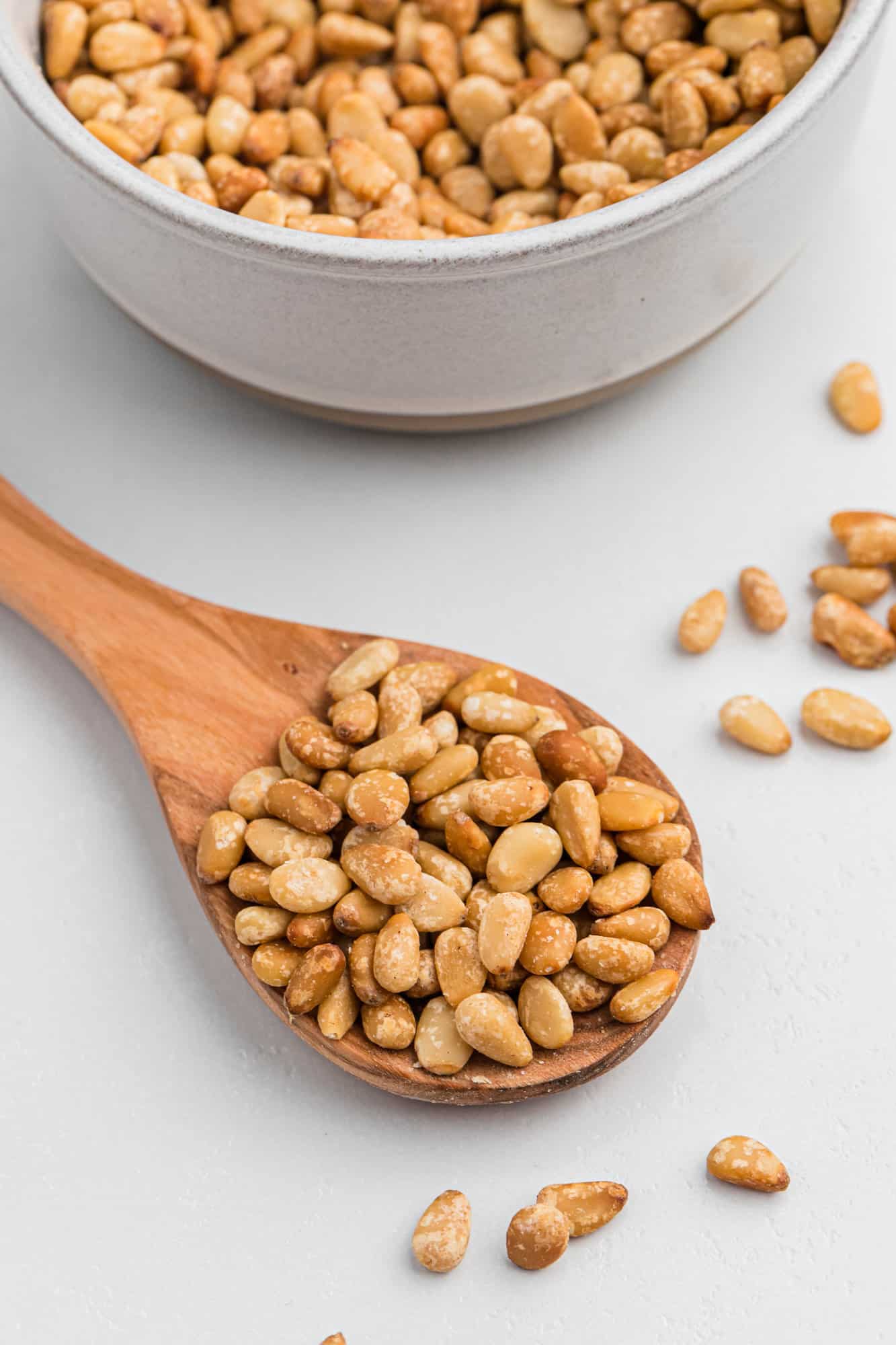 Toasted pine nuts on a small wooden spoon.