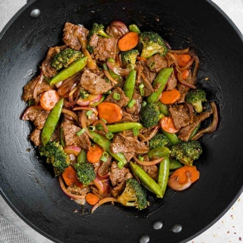Beef and vegetable stir fry in a black wok.