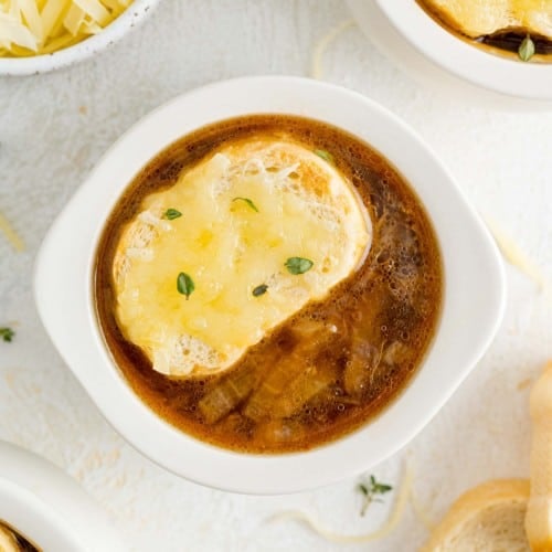 French onion soup in white bowl with bread and cheese topping.