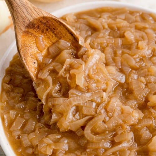 Caramelized onions in a bowl with wooden spoon.