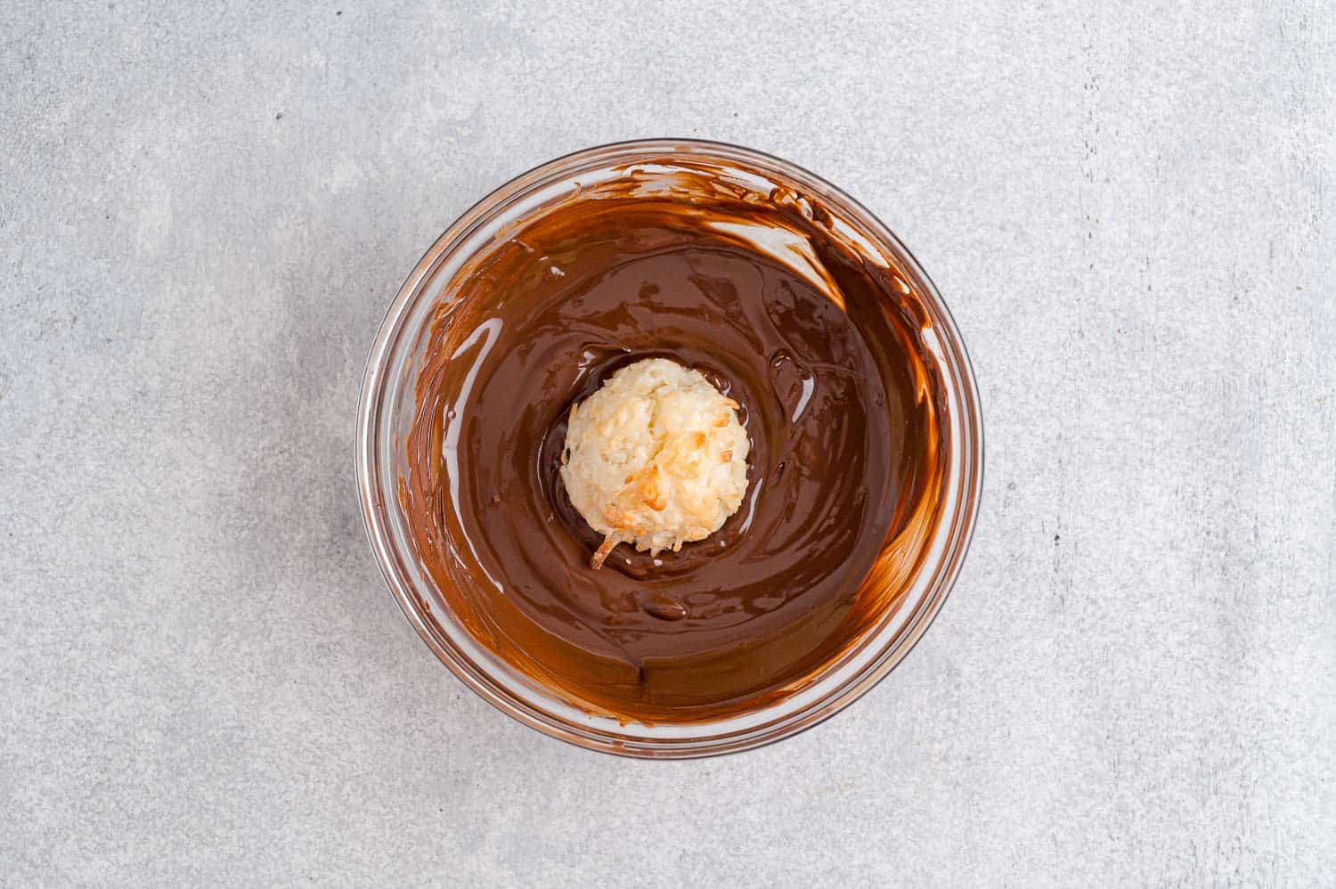 Coconut macaroon being dipped in chocolate.