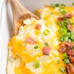 Loaded mashed potato casserole being scooped with a wooden spoon.