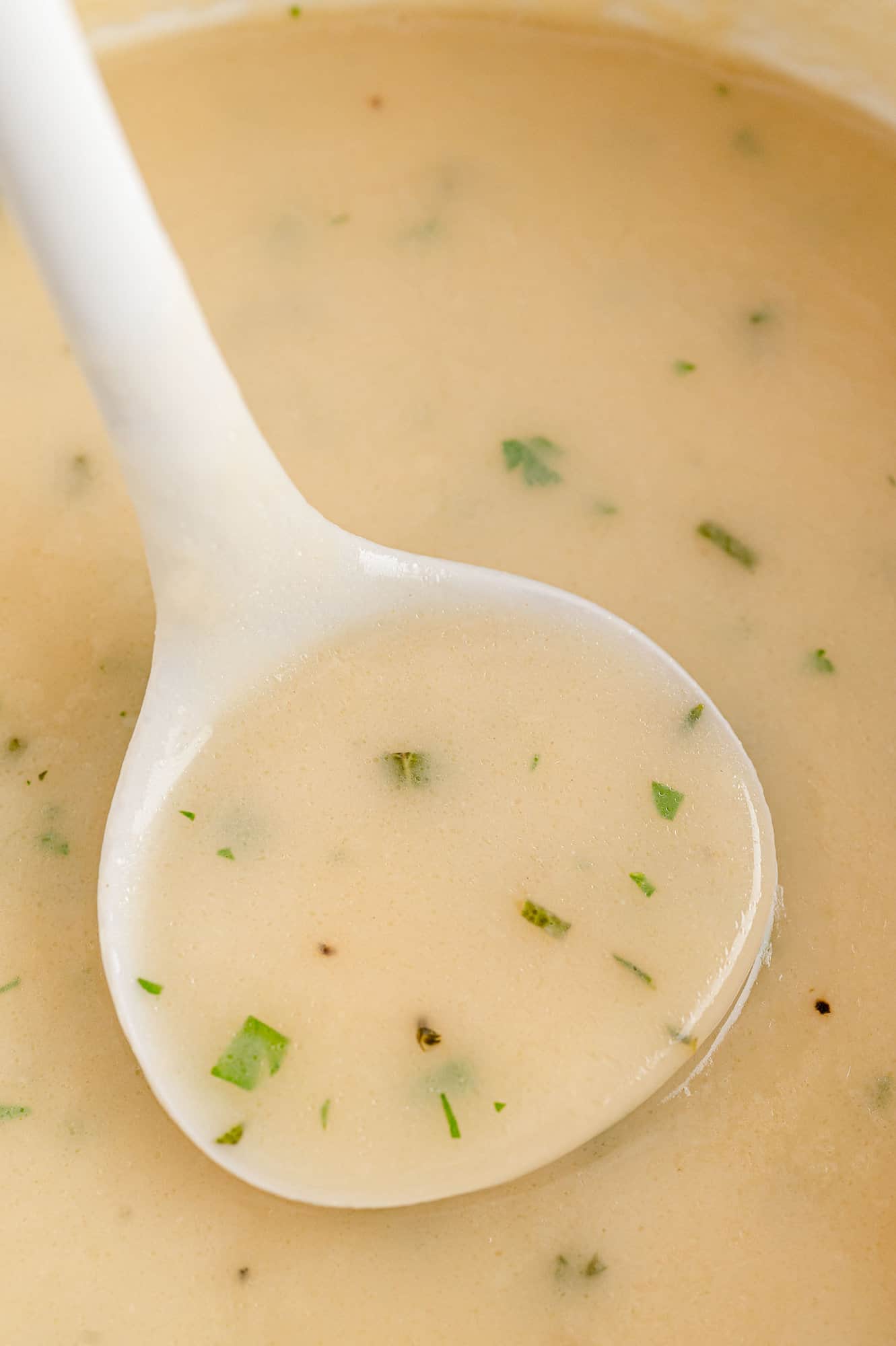Make-ahead turkey gravy in a white ladle.