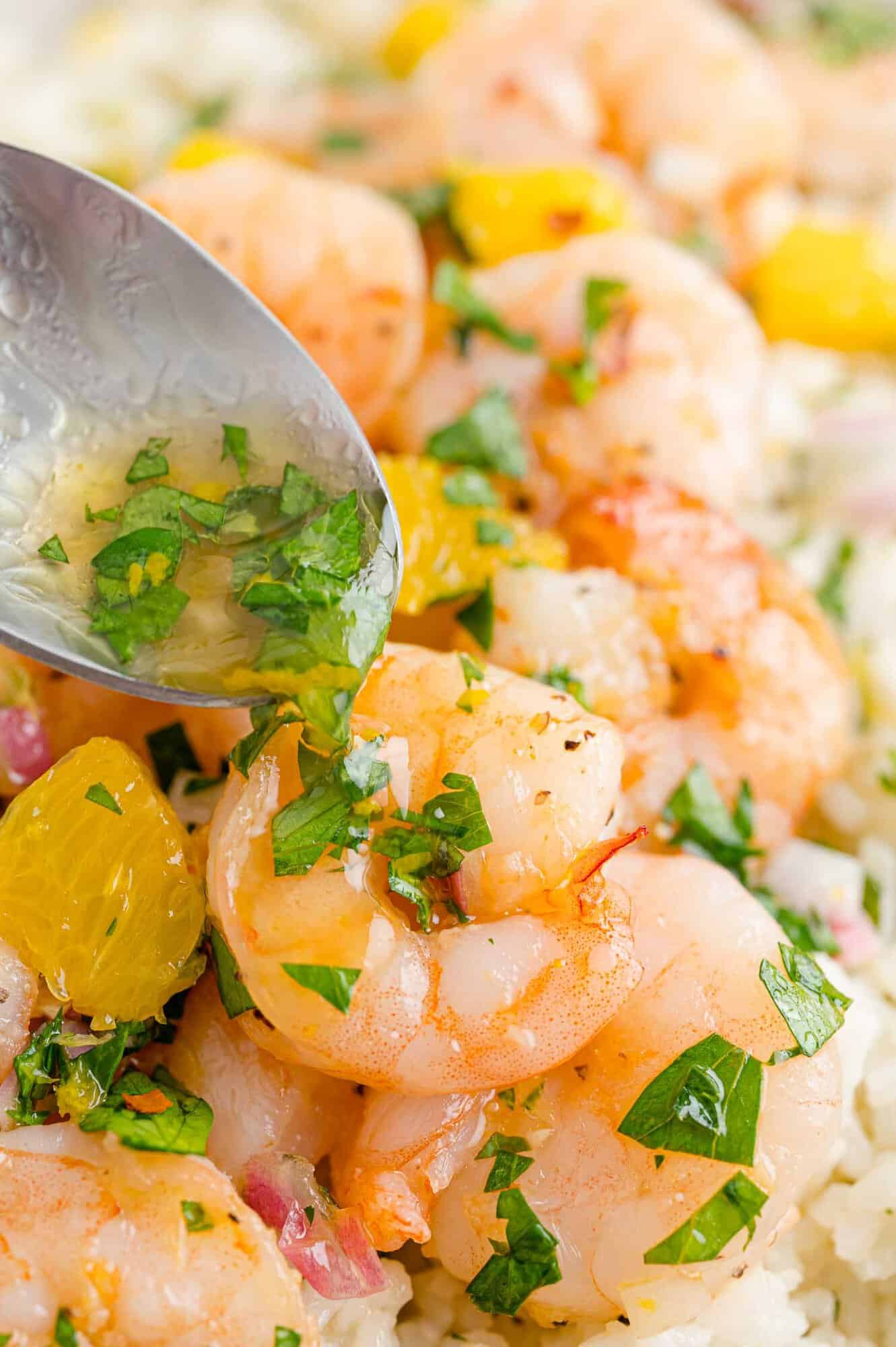 Chimichurri being spooned over shrimp.