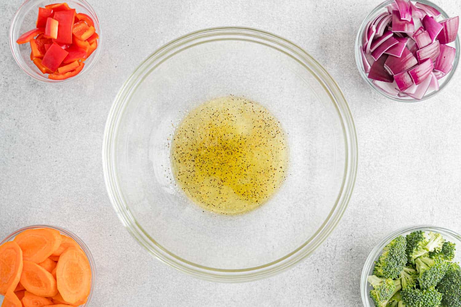 Oil and seasoning in a bowl, surrounded by vegetables.