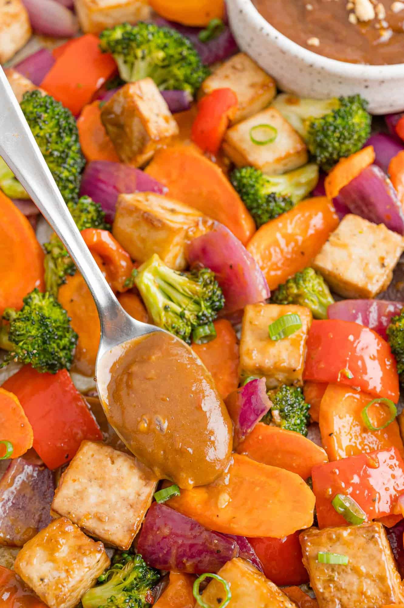 Peanut butter sauce being added to tofu sheet pan dinner.