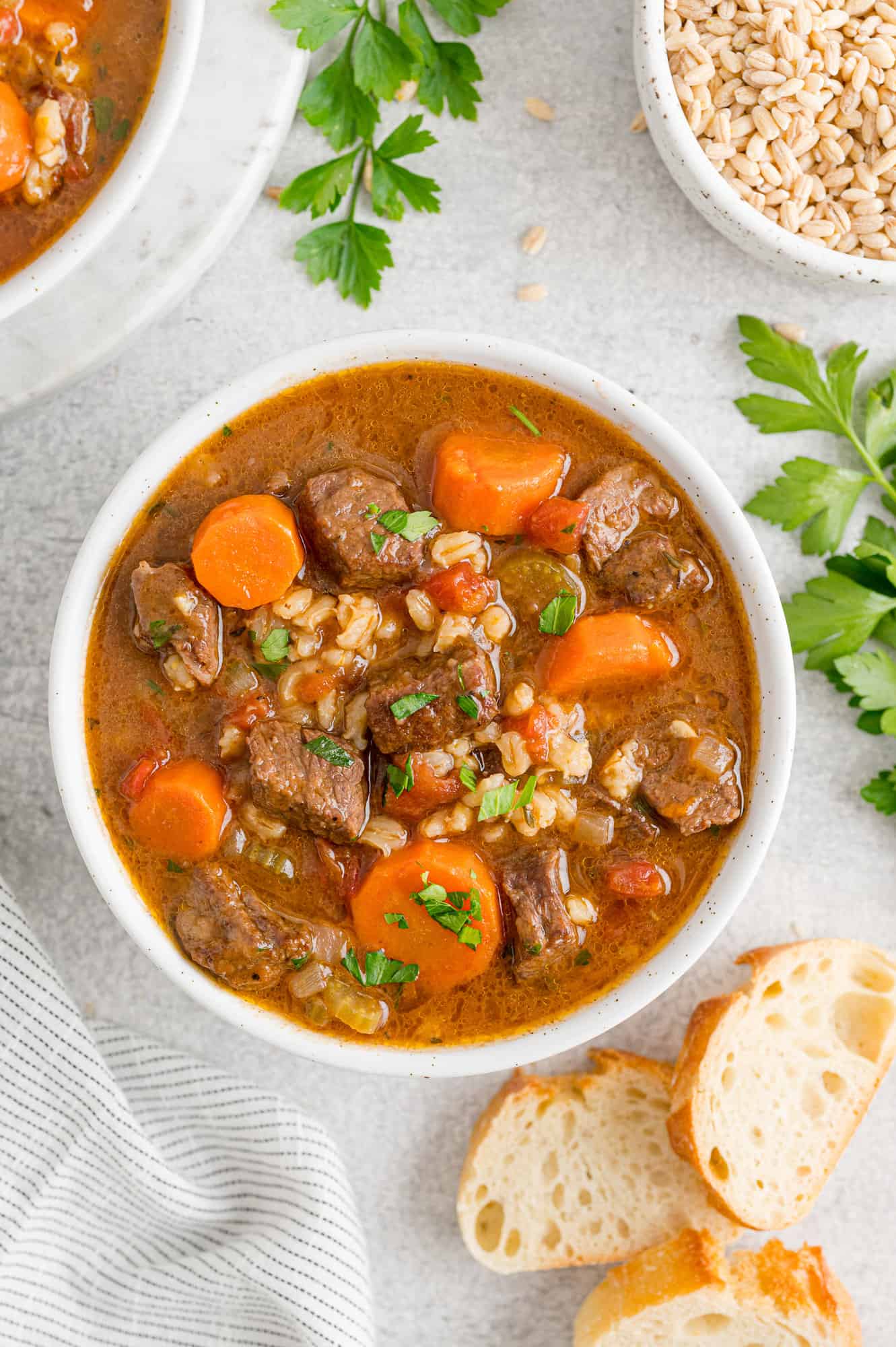 Beef barley soup surrounded by bread and parsley.