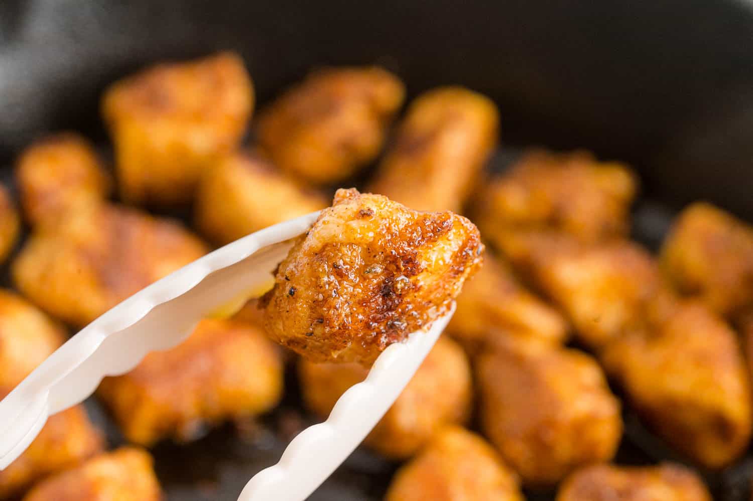 Chicken bites held by tongs.