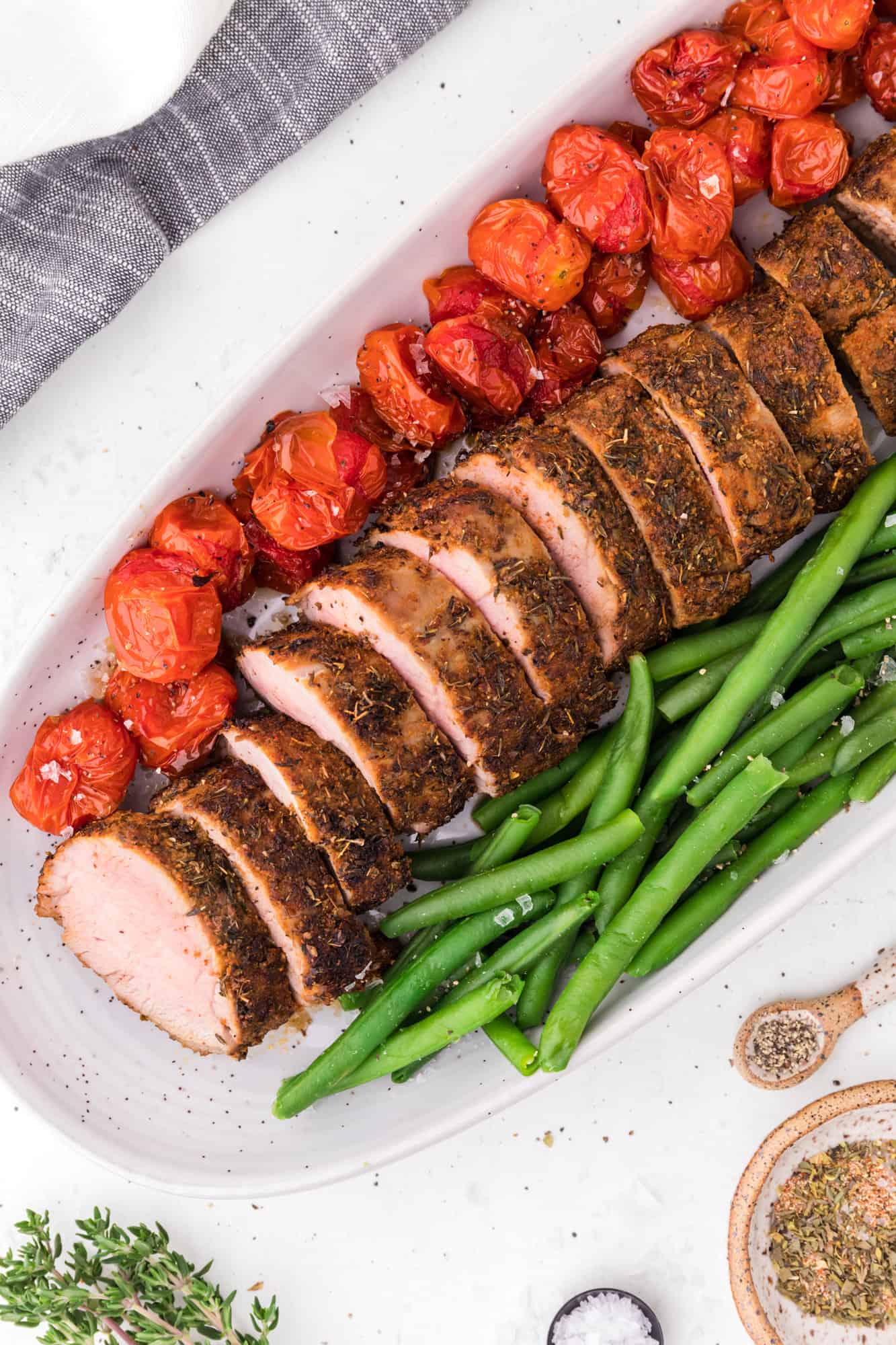 Pork on a platter with green beans and tomatoes.