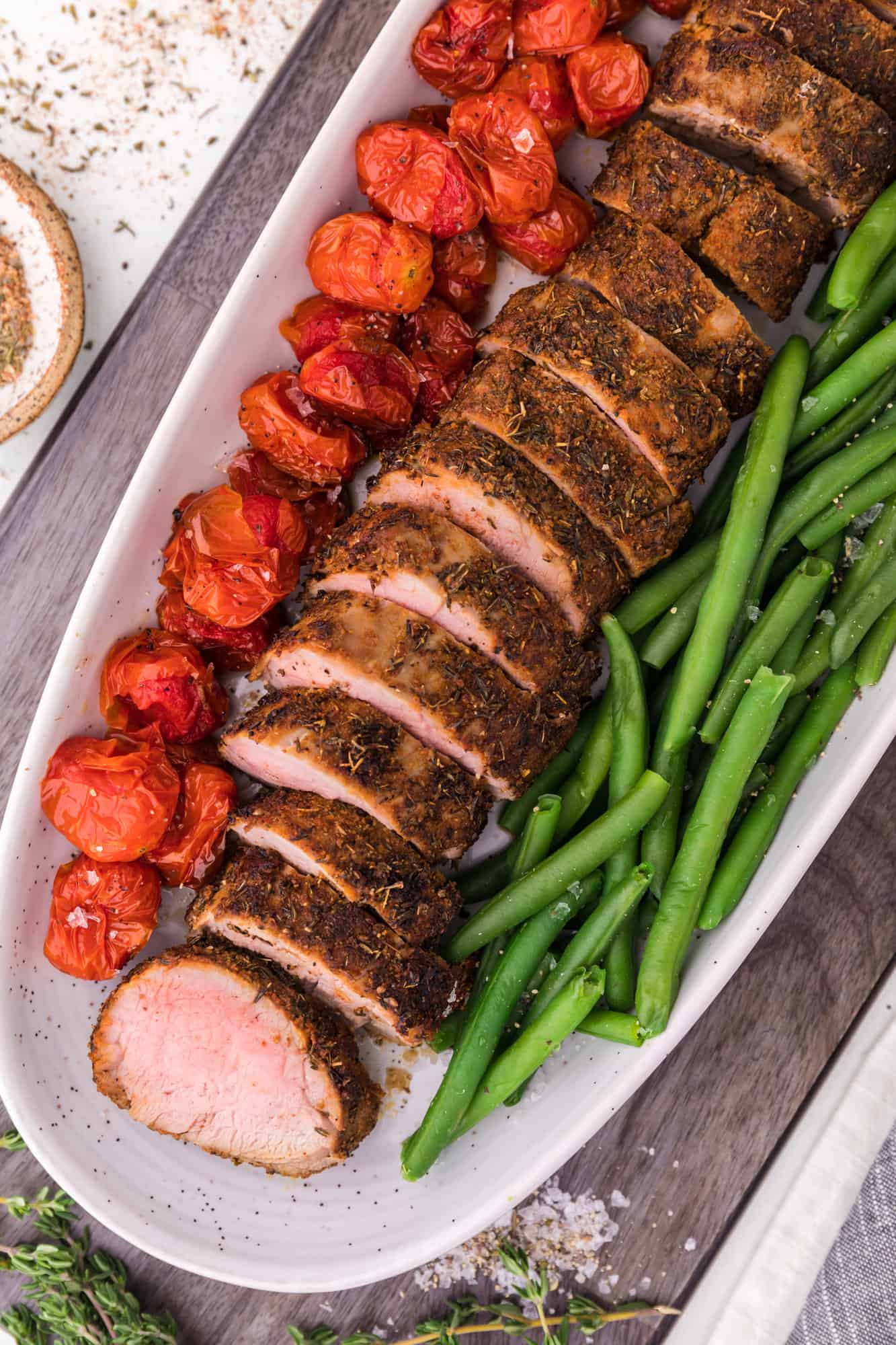 Pork tenderloin on platter with tomatoes and green beans.