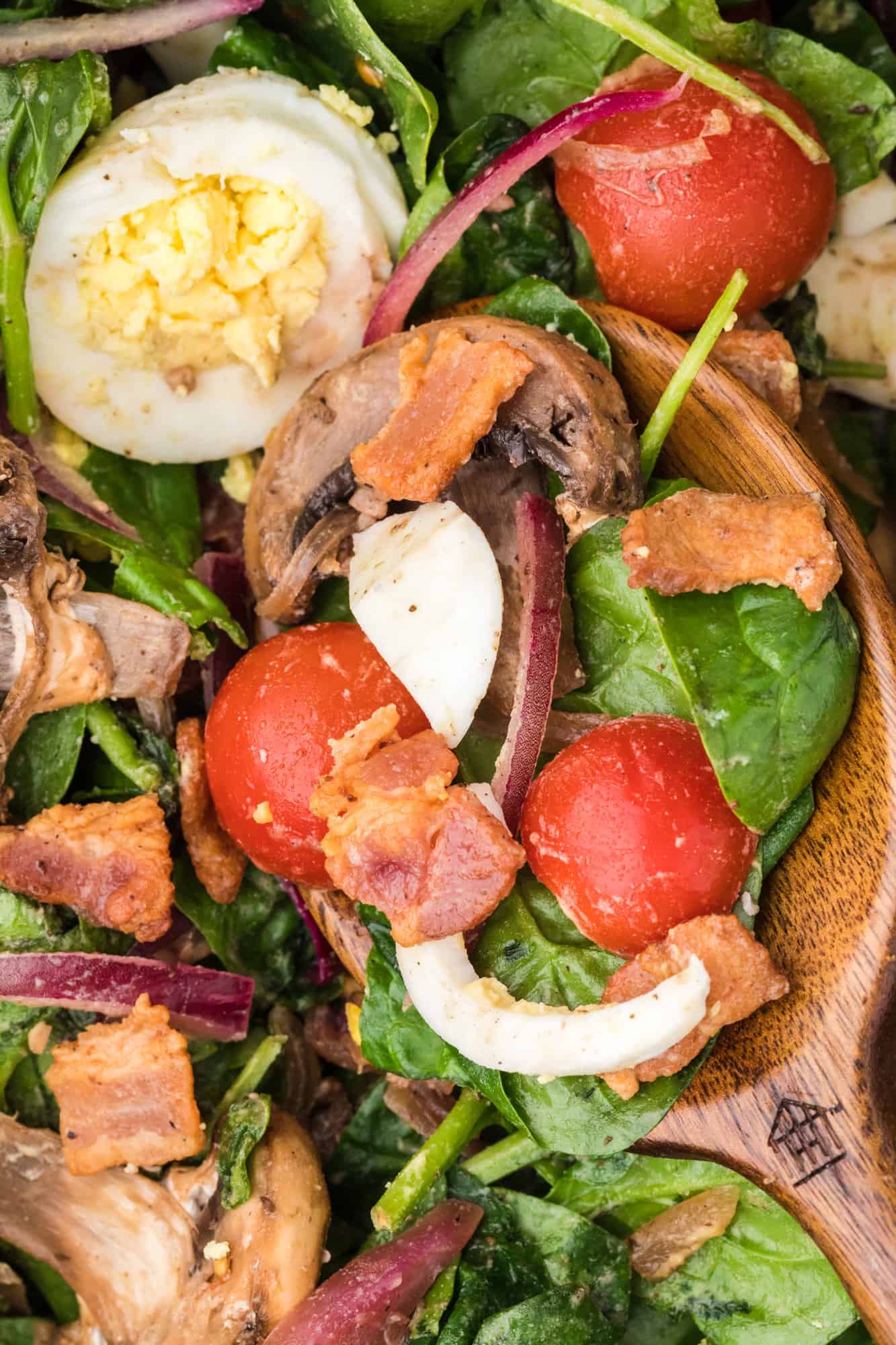 Close up of spinach salad on serving spoon.