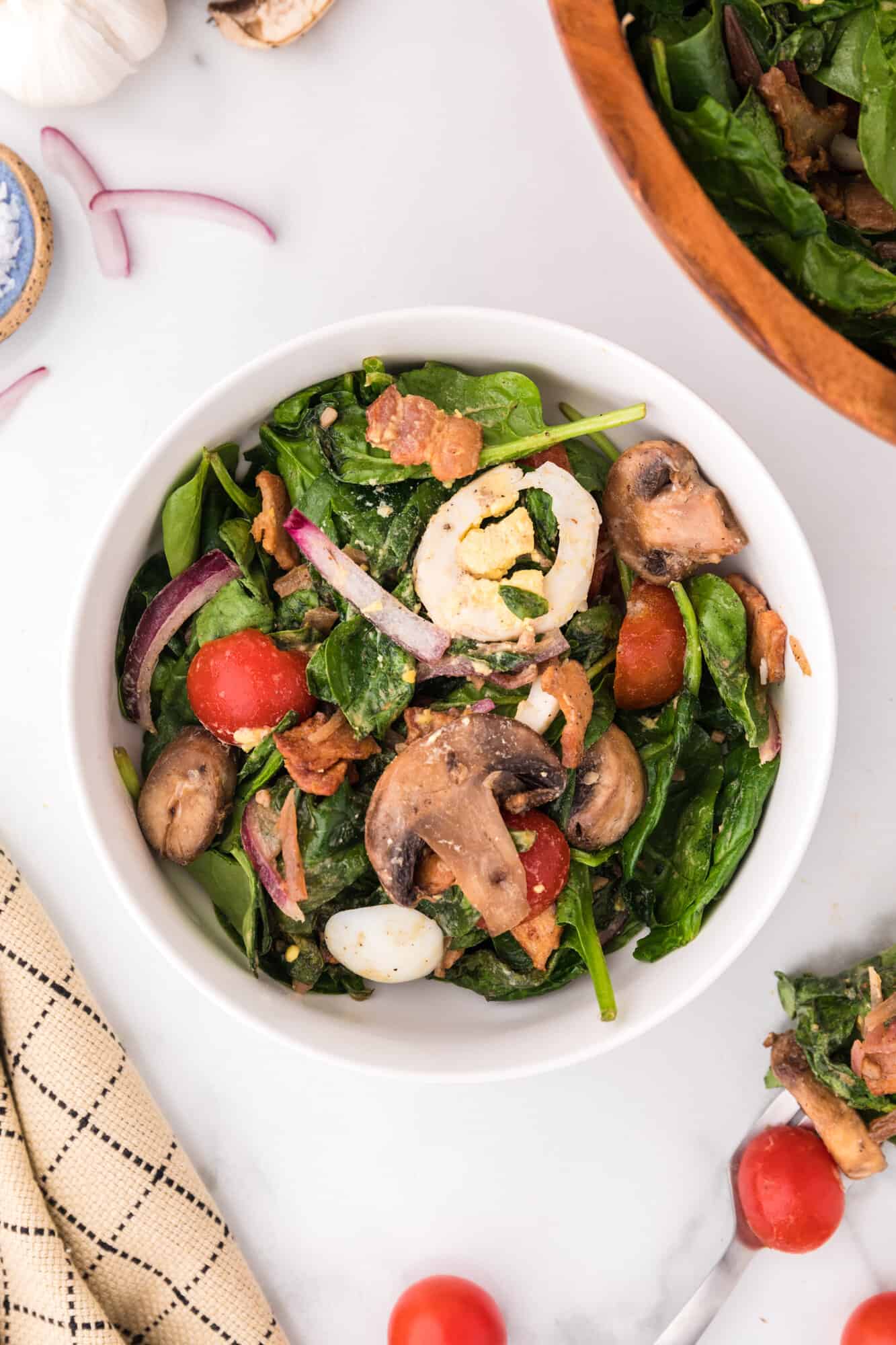 Spinach salad in a small bowl, surrounded by ingredients.